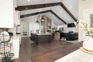 Kitchen with a fireplace, a sink, white cabinetry, an island with sink, and beam ceiling