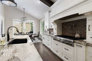 Kitchen with stainless steel gas cooktop, a sink, tasteful backsplash, dark wood-style floors, and lofted ceiling