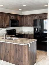 Kitchen featuring black appliances, light stone countertops, dark brown cabinetry, a peninsula, and a textured ceiling