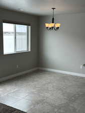 Empty room featuring a chandelier, a textured ceiling, and baseboards