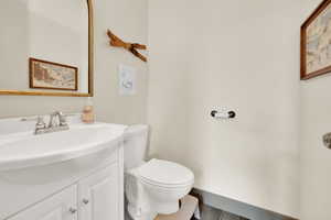 Half bath with vanity, toilet, wood finished floors, and baseboards