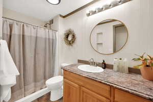 Full bath with vanity, toilet, curtained shower, and a textured ceiling