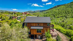 Rear view of property with roof with shingles, a wooded view, a deck with mountain view, a cooling unit, and a chimney