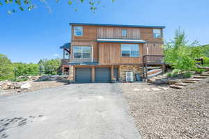 View of front of property with asphalt driveway, stone siding, stairs, and an attached garage
