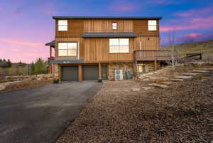 View of front facade with driveway, ac unit, stone siding, an attached garage, and a wooden deck