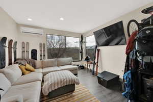 Living room with a wall unit AC, wood finished floors, and recessed lighting