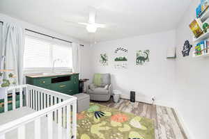 Bedroom featuring light wood-style flooring, a nursery area, baseboards, and a ceiling fan