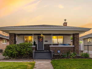 Bungalow-style home featuring brick siding, a lawn, central air condition unit, a porch, and a chimney