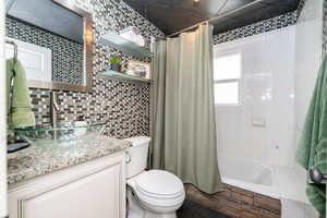 Full bathroom featuring toilet, tile walls, vanity, tiled shower / bath, and backsplash