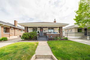Bungalow-style house featuring brick siding, a front lawn, a porch, and cooling unit