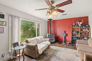 Living area with wood finished floors, a wood stove, and a ceiling fan