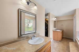 Bathroom featuring two vanities, tile patterned floors, a walk in closet, and baseboards