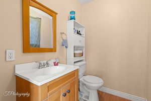 Half bath with vanity, toilet, wood finished floors, and baseboards