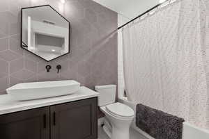 Full bathroom featuring shower / bath combo, visible vents, toilet, tile walls, and vanity