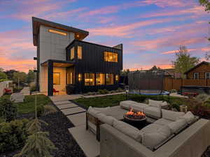 Rear view of property with a trampoline, board and batten siding, a hot tub, a patio, and an outdoor living space with a fire pit
