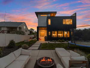 Back of house at dusk with an outdoor living space with a fire pit, a trampoline, board and batten siding, and fence
