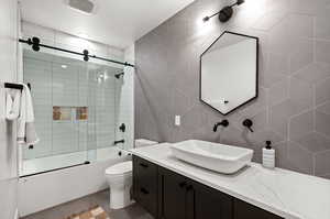 Full bath with shower / bath combination with glass door, vanity, tile patterned floors, toilet, and backsplash