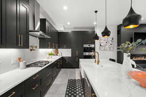 Kitchen with a sink, dark cabinetry, wall chimney exhaust hood, backsplash, and appliances with stainless steel finishes