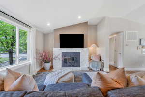 Living area featuring lofted ceiling, wood finished floors, a glass covered fireplace, baseboards, and recessed lighting