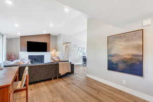 Living room featuring baseboards, a fireplace, light wood finished floors, lofted ceiling, and recessed lighting