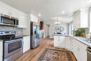 Kitchen with appliances with stainless steel finishes, a chandelier, white cabinetry, a peninsula, and lofted ceiling