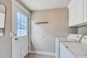 Laundry area featuring washing machine and clothes dryer, cabinet space, baseboards, and light wood-type flooring