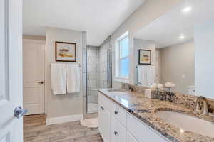 Bathroom featuring a shower stall, wood finish floors, baseboards, double vanity, and toilet