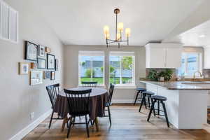 Dining area with light wood-type flooring, healthy amount of natural light, baseboards, and a chandelier