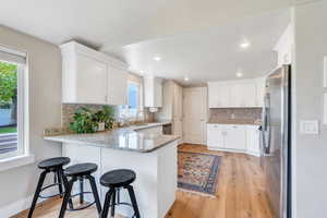 Kitchen with appliances with stainless steel finishes, a peninsula, decorative backsplash, a sink, and light stone counters