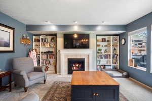 Living area with light colored carpet, a tiled fireplace, and baseboards