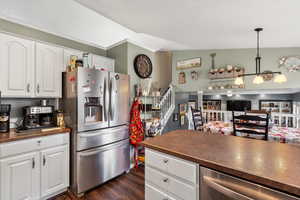 Kitchen featuring stainless steel appliances, dark countertops, dark wood-style flooring, white cabinetry, and decorative light fixtures