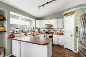 Kitchen featuring stainless steel appliances, a sink, dark countertops, white cabinetry, and lofted ceiling