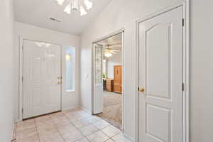 Foyer with a chandelier, light tile patterned floors, vaulted ceiling, baseboards, and light carpet