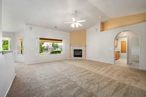 Unfurnished living room with light colored carpet, a ceiling fan, healthy amount of natural light, a fireplace, and high vaulted ceiling