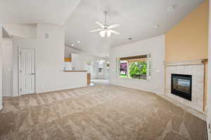 Unfurnished living room with carpet floors, a tiled fireplace, ceiling fan, baseboards, and high vaulted ceiling