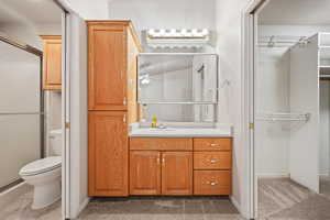 Full bath featuring toilet, vanity, a shower with door, baseboards, and a spacious closet