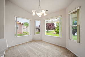 Carpeted spare room featuring a chandelier, baseboards, and vaulted ceiling