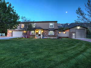 View of front of property featuring an attached garage, driveway, a front yard, stucco siding, and stone siding