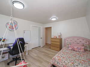 Bedroom featuring light wood finished floors, a closet, an office area, and a textured ceiling