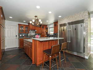 Kitchen with built in refrigerator, a chandelier, under cabinet range hood, decorative backsplash, and a kitchen island