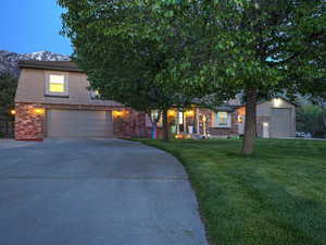 View of front of property featuring a front lawn, stucco siding, driveway, a garage, and stone siding