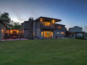 Back of house at dusk featuring a balcony, a lawn, a gazebo, a patio, and a chimney