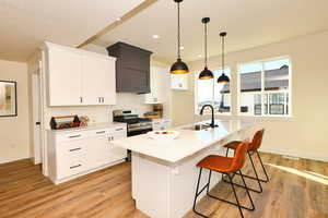 Kitchen featuring a sink, stainless steel range with gas cooktop, light wood finished floors, white cabinets, and recessed lighting