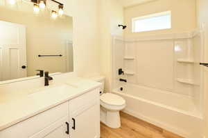 Bathroom with wood finished floors, toilet, vanity, and shower / bath combination