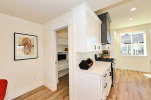 Kitchen with stainless steel range with gas cooktop, white cabinets, light wood-style flooring, light countertops, and baseboards