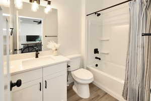 Full bathroom with wood finished floors, toilet, shower / bathtub combination with curtain, and vanity