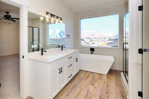 Bathroom featuring a shower stall, a soaking tub, double vanity, wood finished floors, and ceiling fan