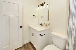Bathroom featuring toilet, wood finished floors, vanity, and baseboards