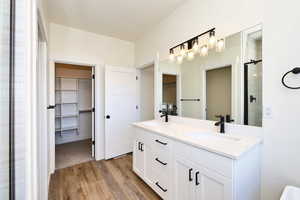 Bathroom with a walk in closet, wood finished floors, a stall shower, and double vanity