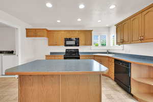 Kitchen with black appliances, washer and dryer, a sink, recessed lighting, and a kitchen island